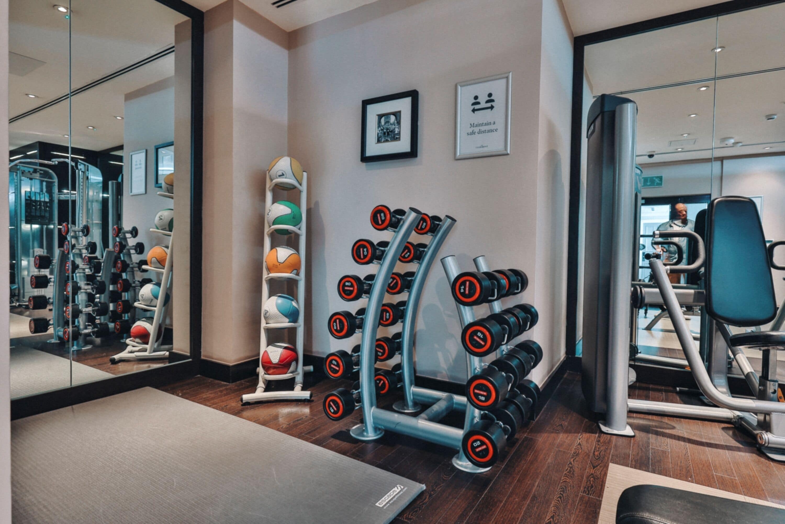 A gym with exercise equipment, a mirror, and a wall with a framed picture and a sign.