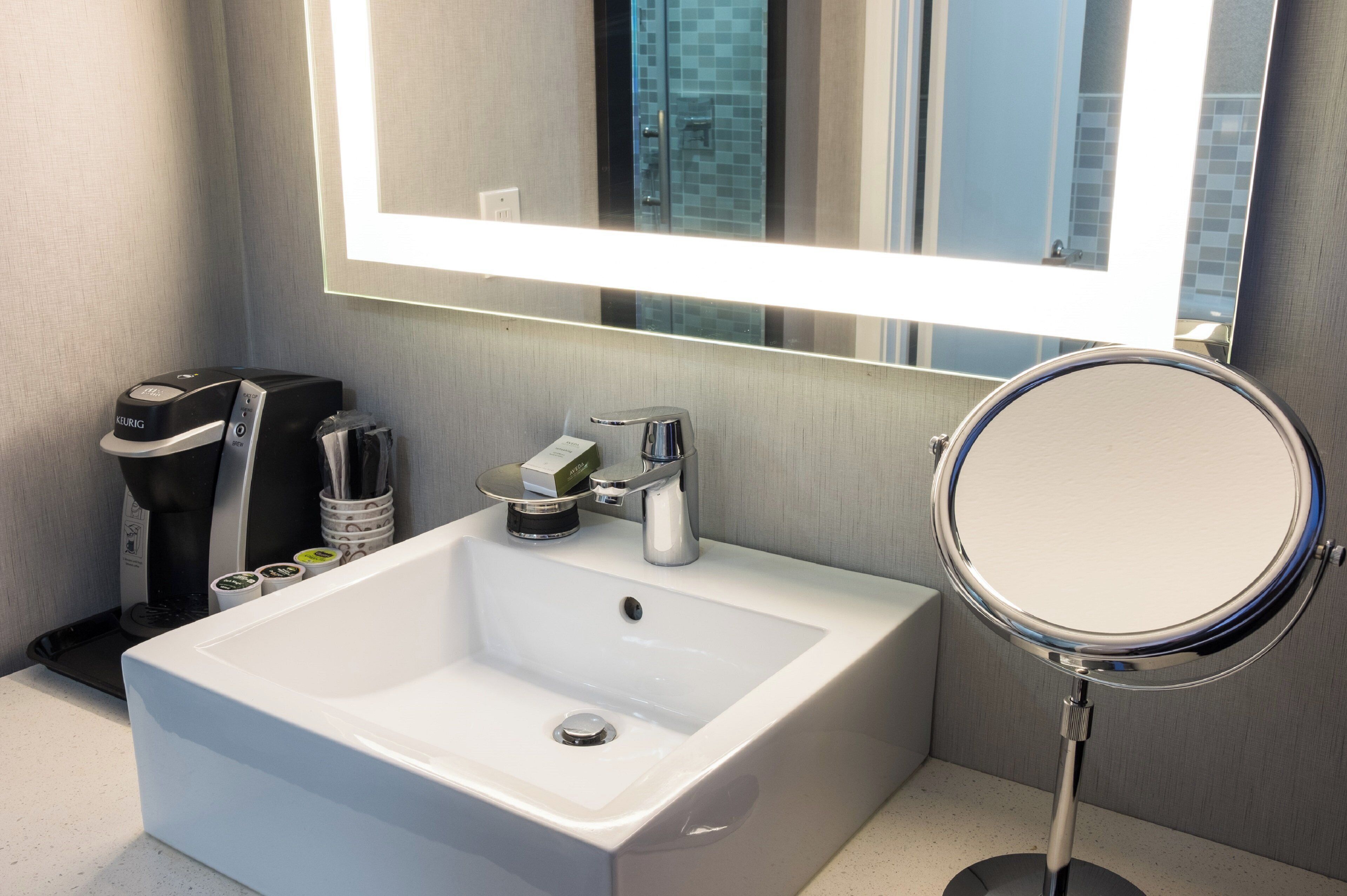 A modern bathroom with a white sink, a mirror, and a coffee machine.