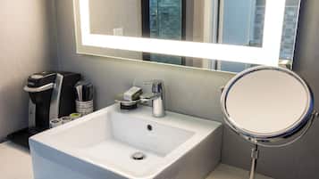 A modern bathroom with a white sink, a mirror, and a coffee machine.