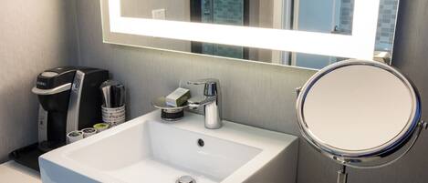 A modern bathroom with a white sink, a mirror, and a coffee machine.