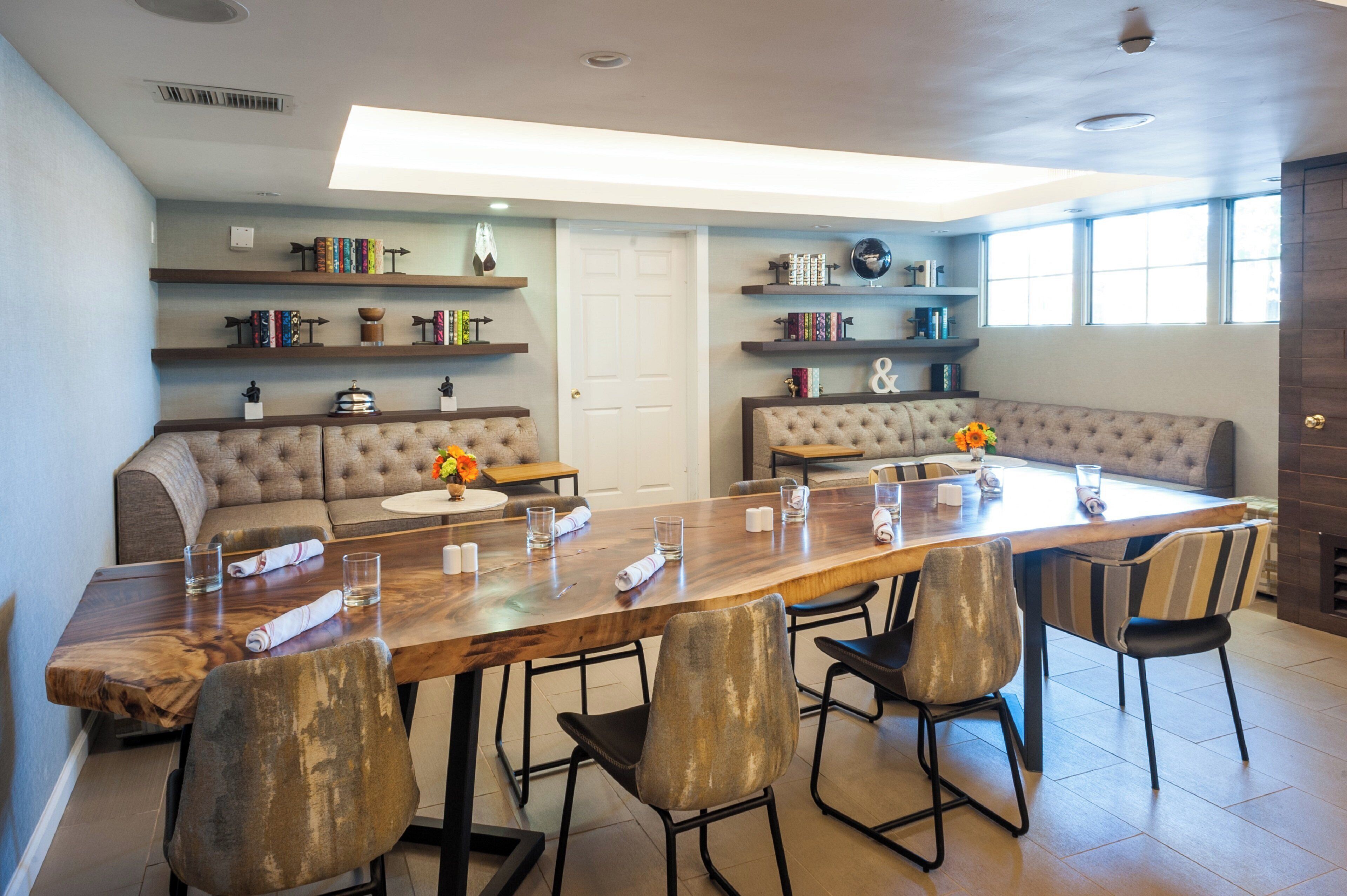 A modern dining area with a long wooden table, cushioned seating, and bookshelves with decorative items.