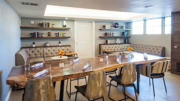 A modern dining area with a long wooden table, cushioned seating, and bookshelves with decorative items.