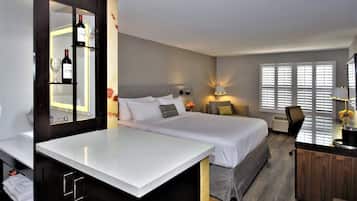 A hotel room with a bed, a desk, a mirror, and a minibar.