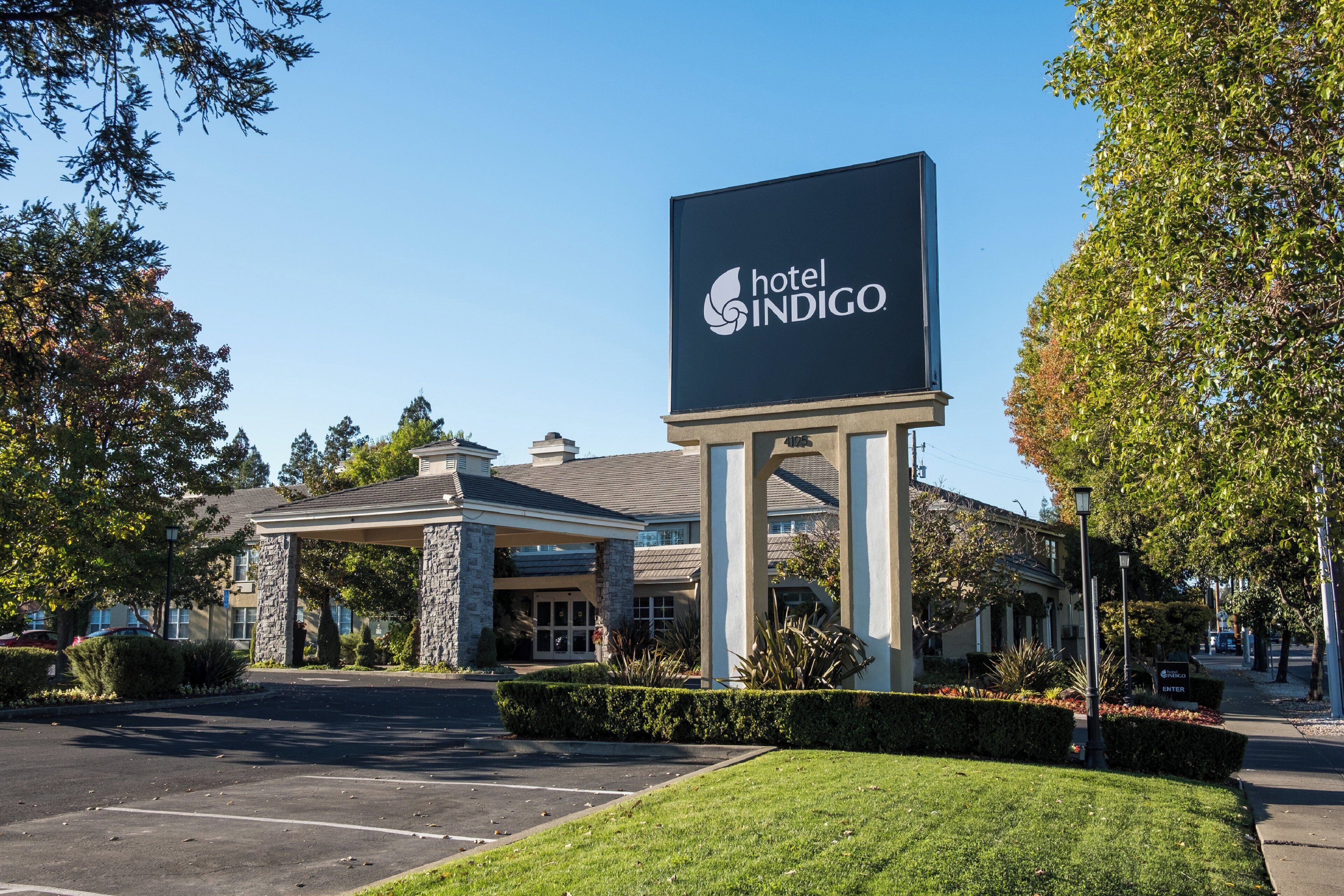 A hotel entrance with a large sign, a covered parking area, and well-maintained landscaping.