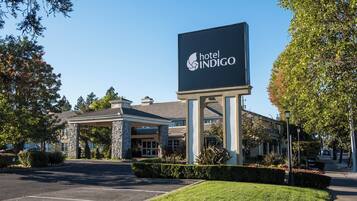 A hotel entrance with a large sign, a covered parking area, and well-maintained landscaping.