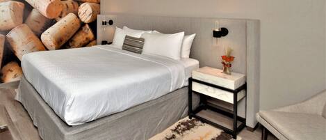 Un dormitorio moderno con una cama grande, una mesita de noche con un florero y una lámpara de pared.