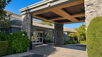 A modern building with a covered entrance, stone pillars, and a well-maintained garden.