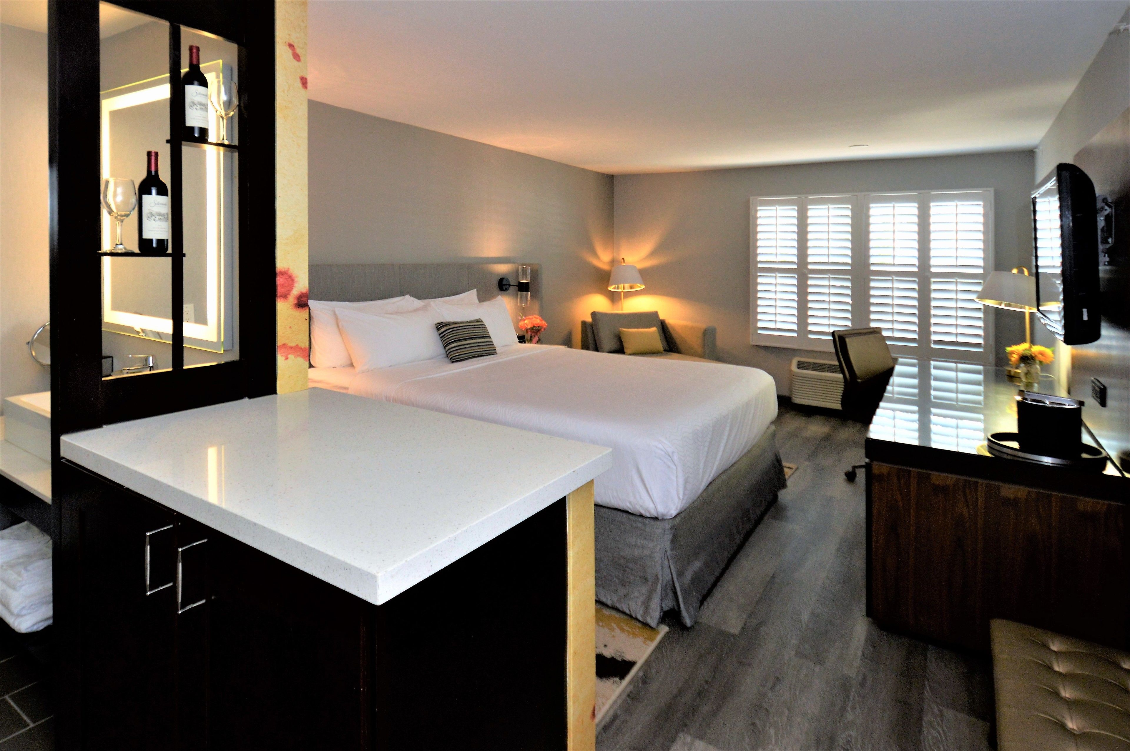 Une chambre d’hôtel avec un grand lit, un bureau, un miroir et une fenêtre avec des stores.