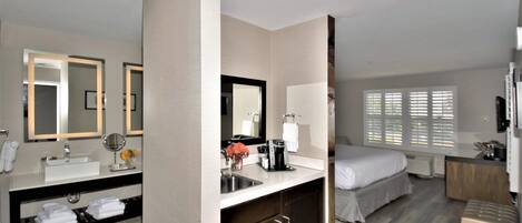 A modern hotel room with a bathroom, a bed, and a desk area.