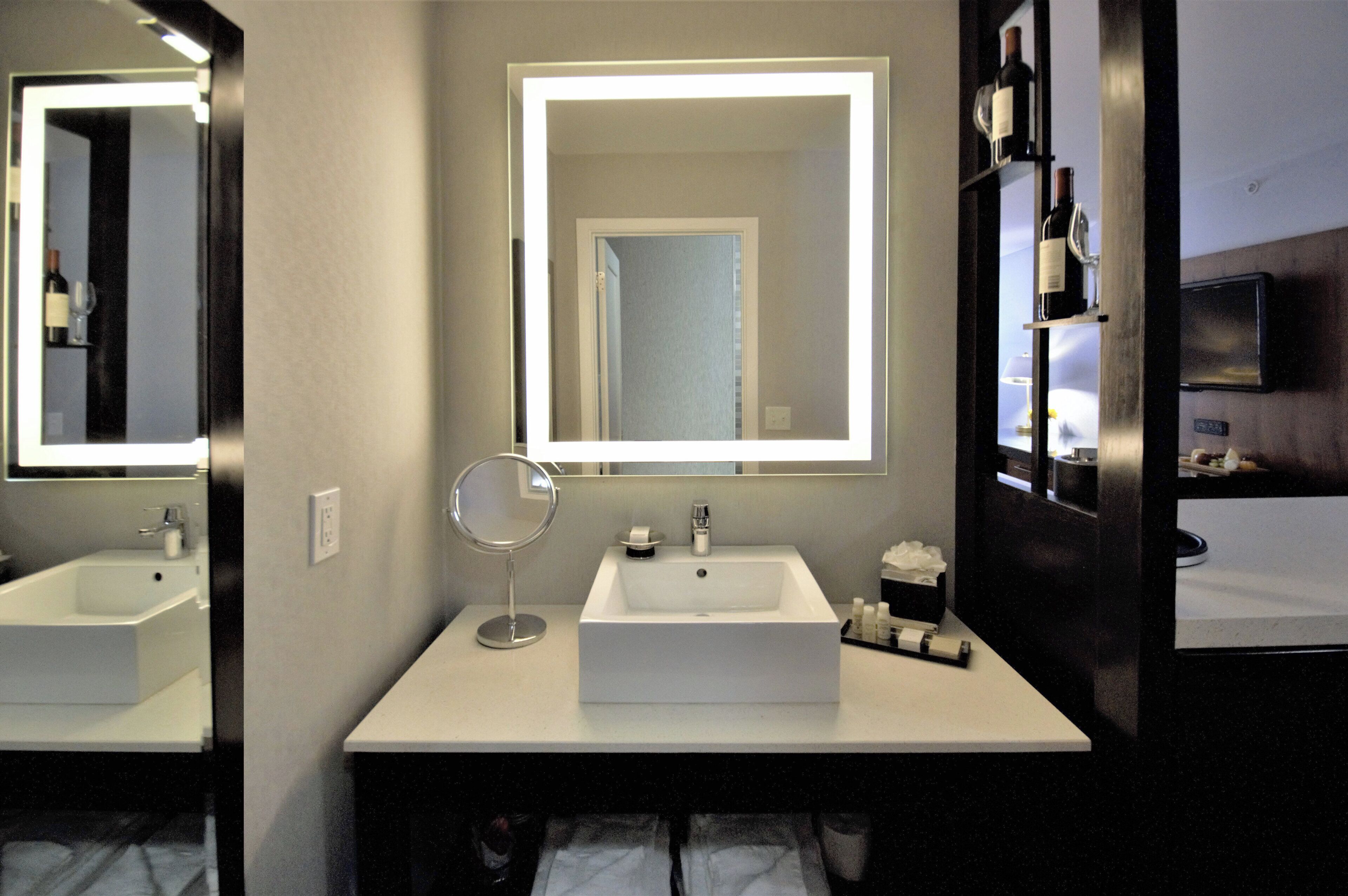 A modern bathroom with two sinks, a round mirror, and a large mirror above the sink.