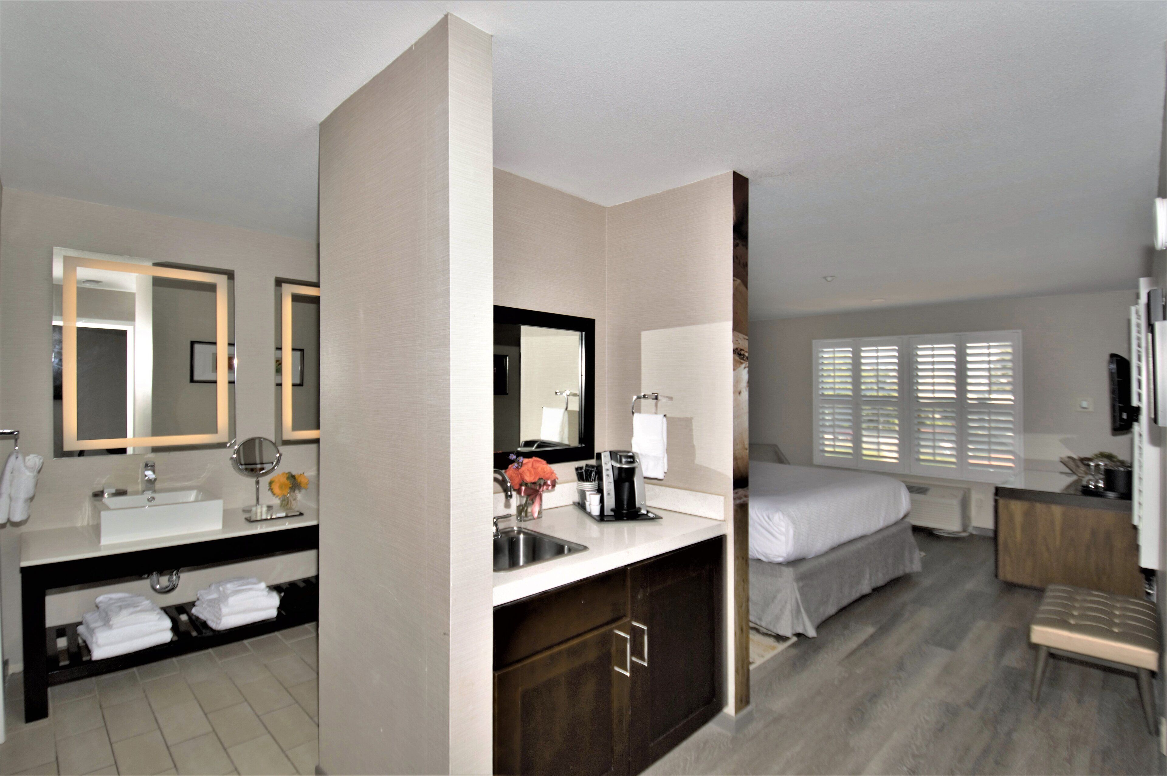 A hotel room with a bathroom, a bed, a desk, and a window.