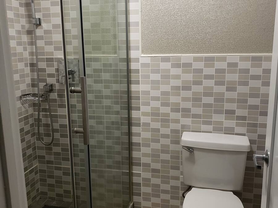 Kylpyhuone, jossa on lasiseinällä varustettu suihku, wc ja laatoitetut seinät.