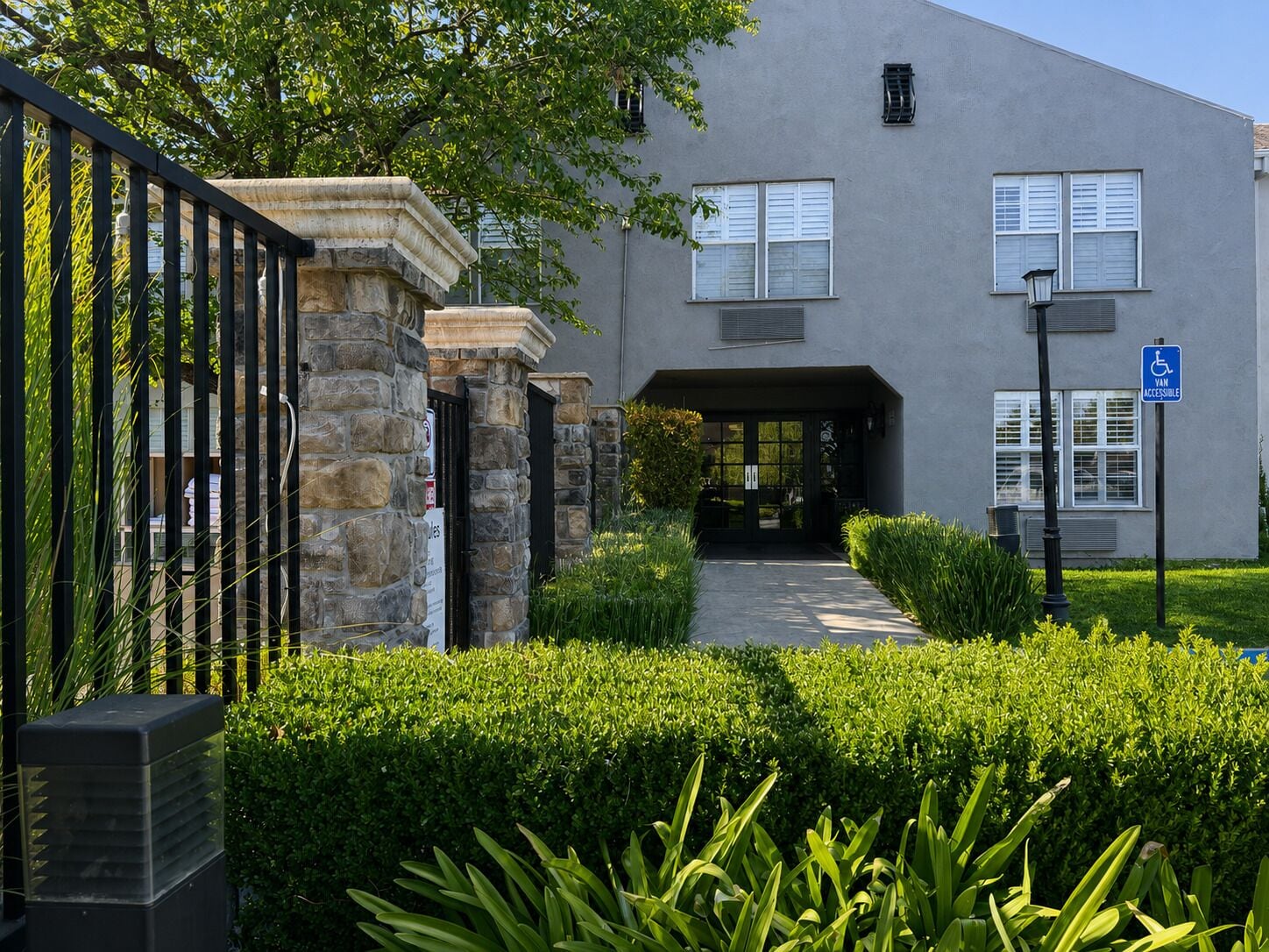 A building with a stone entrance, a van accessible sign, and a well-maintained hedge in the foreground.