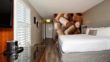 A hotel room with a bed, a TV mounted on the wall, a wine glass and tumbler on a tray, and a wall with a corkscrew image.