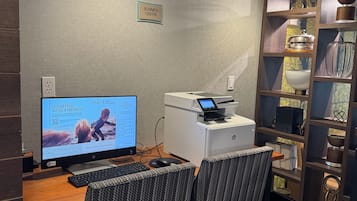A hotel business center with a desktop computer, printer, and seating area.