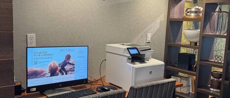 A hotel business center with a desktop computer, printer, and seating area.