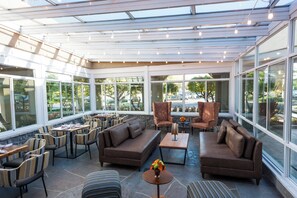 A sunlit indoor patio with seating and tables, large windows, and a view of the outdoors. - Hotel Indigo Napa Valley by IHG (Napa)