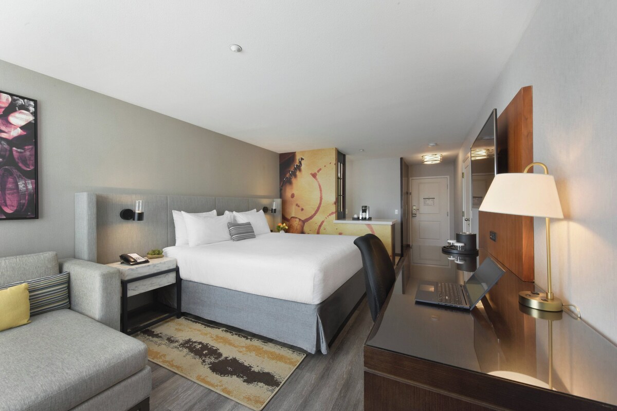 Une chambre d’hôtel moderne avec un grand lit, un bureau, un ordinateur portable et une table de chevet avec une lampe.