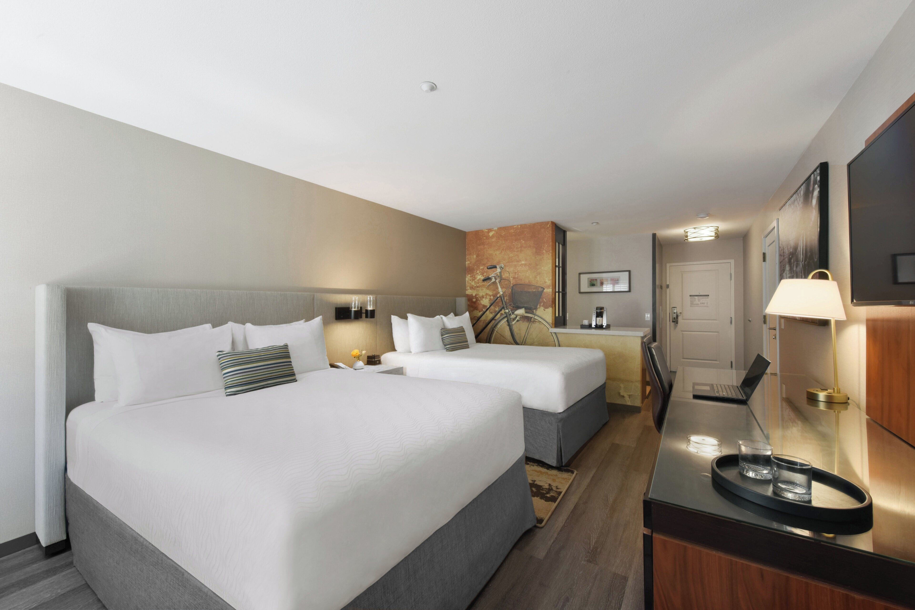 A hotel room with two beds, a desk with a laptop, a chair, and a small table with a tray.