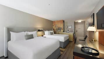 A hotel room with two beds, a desk with a laptop, a chair, and a small table with a tray.