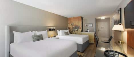 A hotel room with two beds, a desk with a laptop, a chair, and a small table with a tray.
