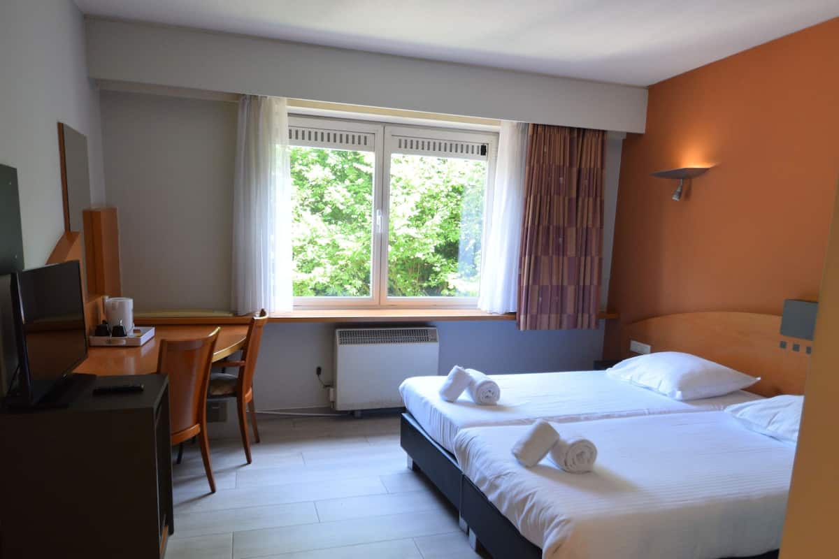 A hotel room with a bed, a desk, a chair, and a window with curtains.