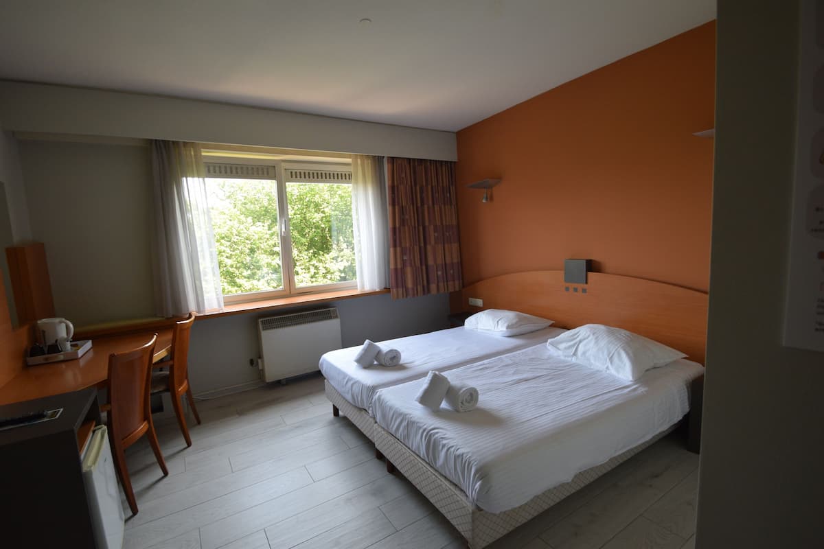 A hotel room with two beds, a desk, and a window with curtains.