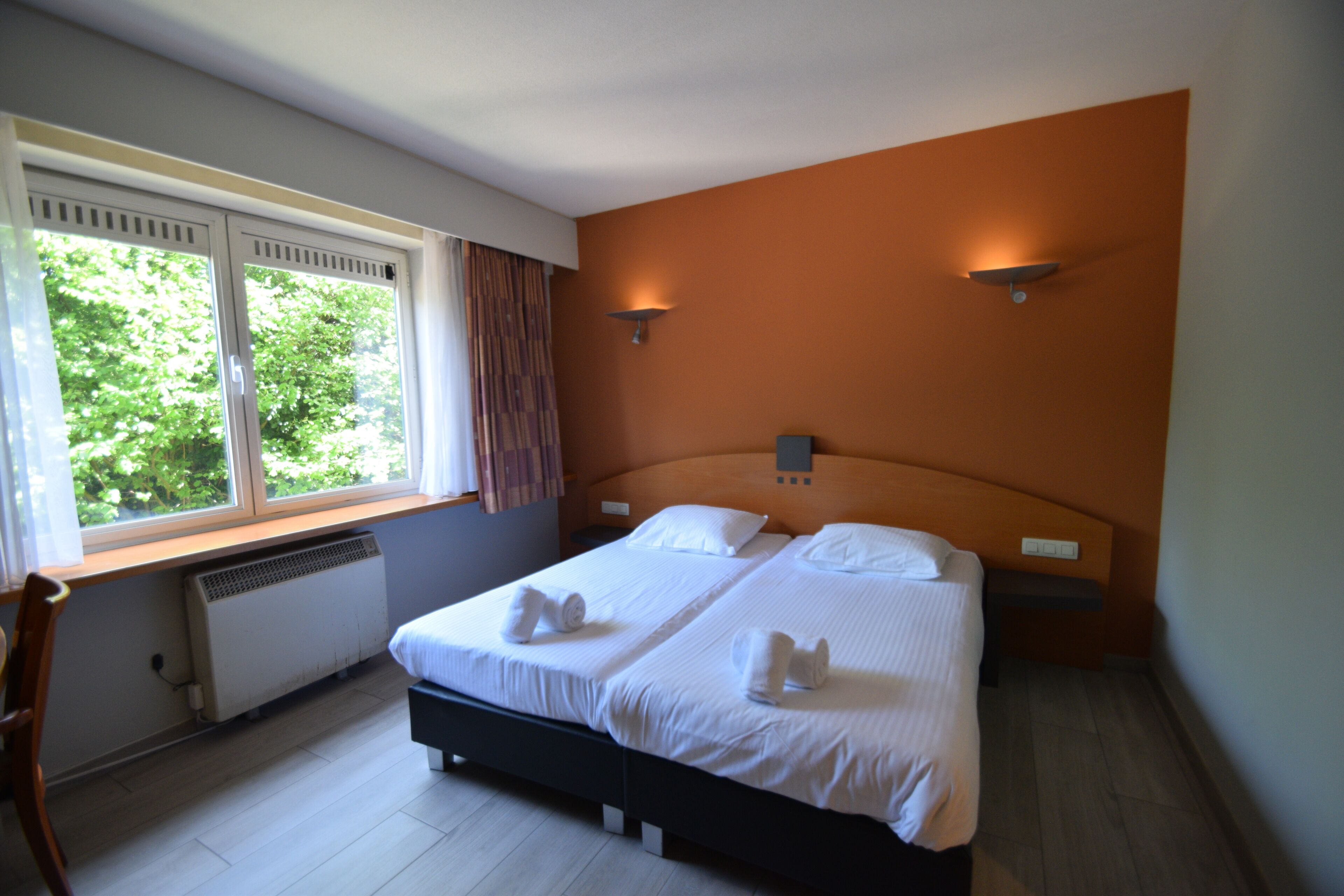 A double bed with white linens and towels, a window with curtains, and a radiator.