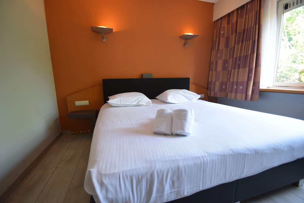 A neatly made bed with white linens and pillows, a dark headboard, and two wall-mounted light fixtures.