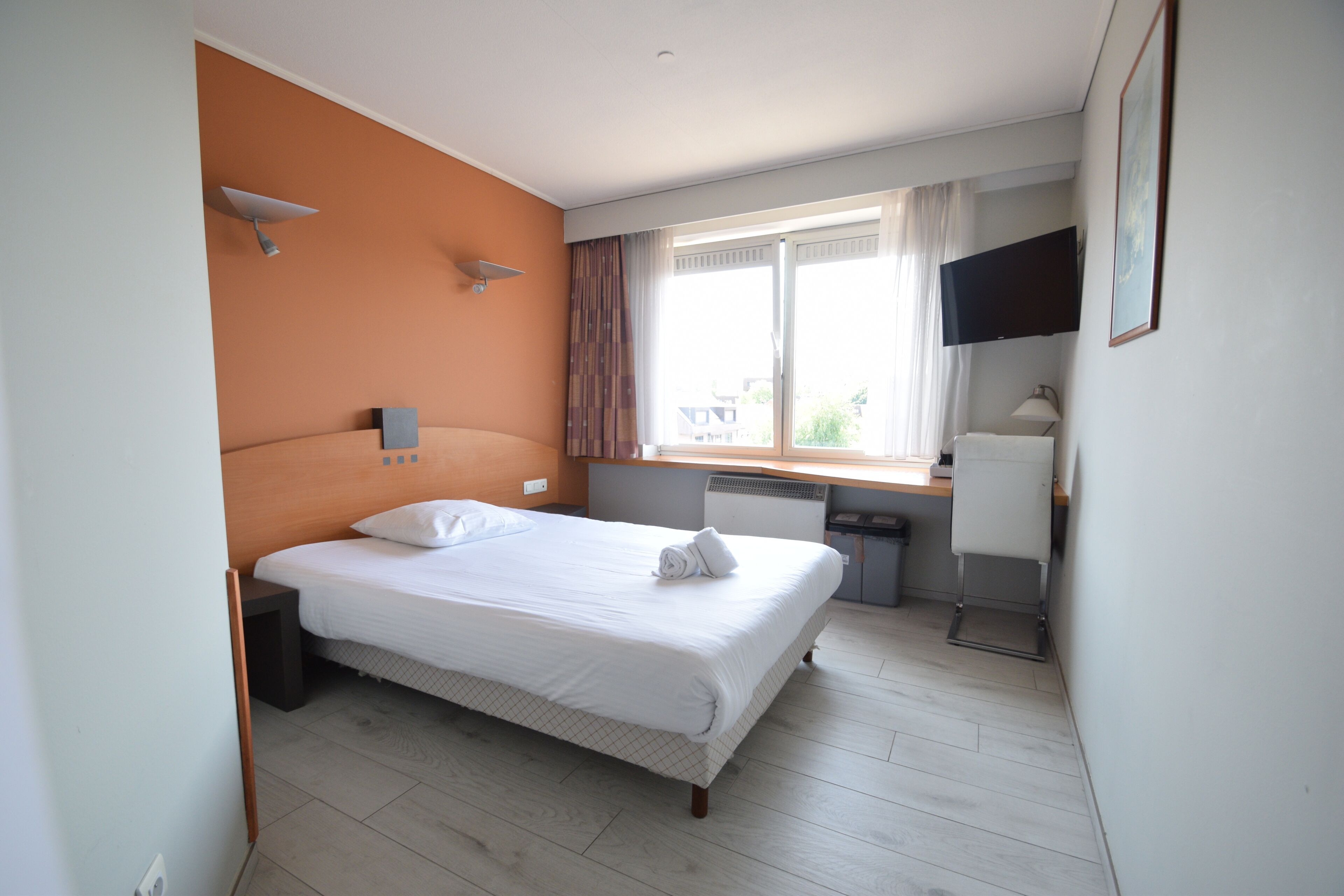 Une chambre d’hôtel avec un lit, un bureau, une chaise, une télévision et une fenêtre avec des rideaux.