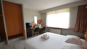 A hotel room with a bed, a desk with a computer, a chair, and a wardrobe. - Sleep & Go Brussels Expo (Grimbergen)
