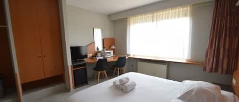 Una habitación de hotel con cama, escritorio con computadora, silla y armario.