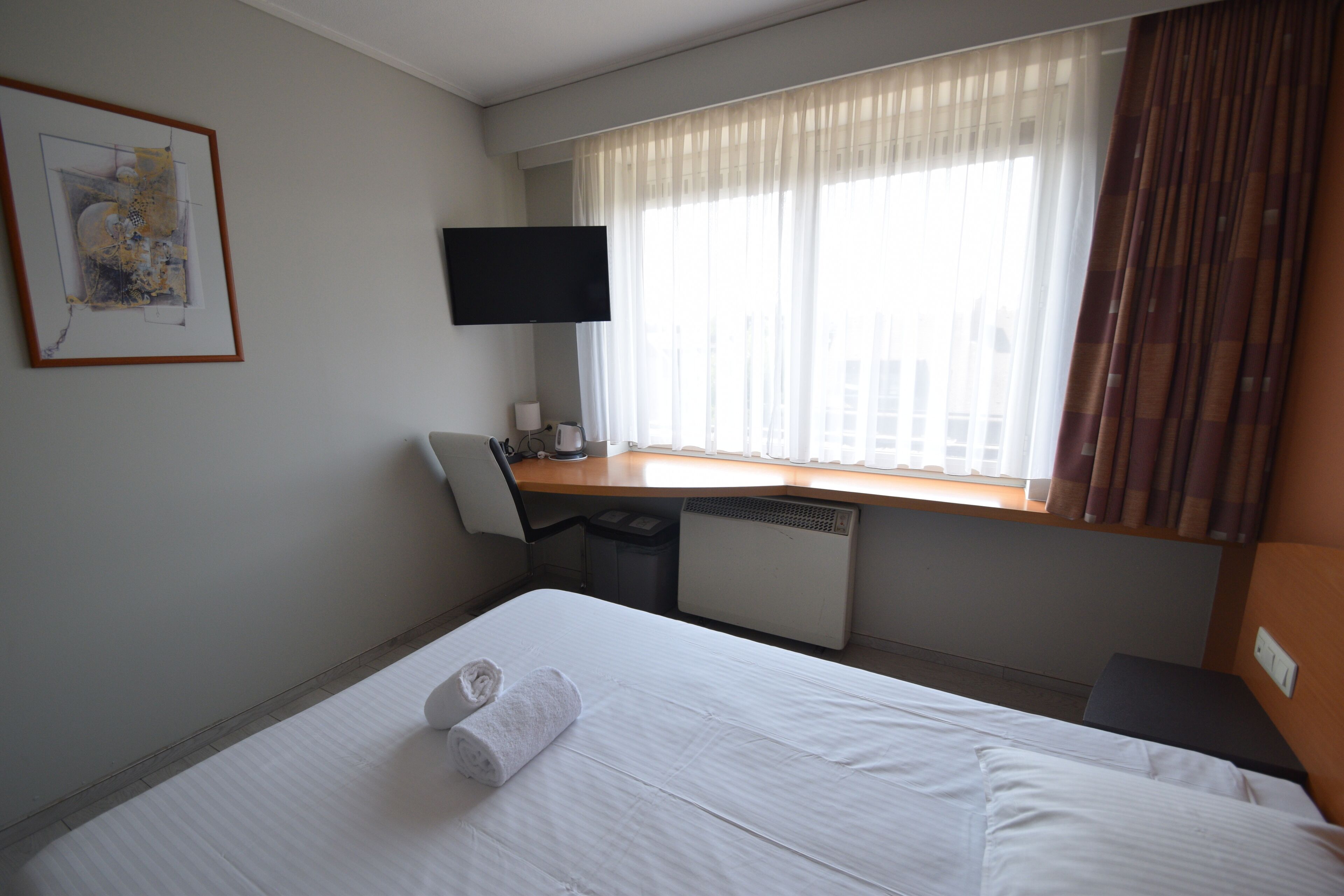 A hotel room with a bed, a desk, a chair, a television, and a window with curtains.