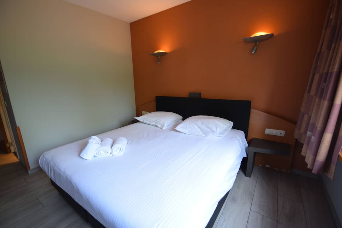 A neatly made bed with white linens and towels, a wooden headboard, and two wall-mounted lamps.