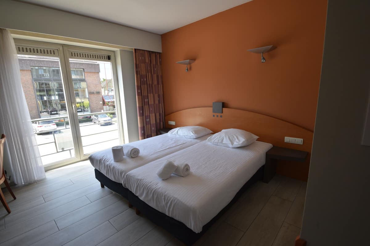 A hotel room with a large bed, a desk, and a view of the street through the sliding doors.