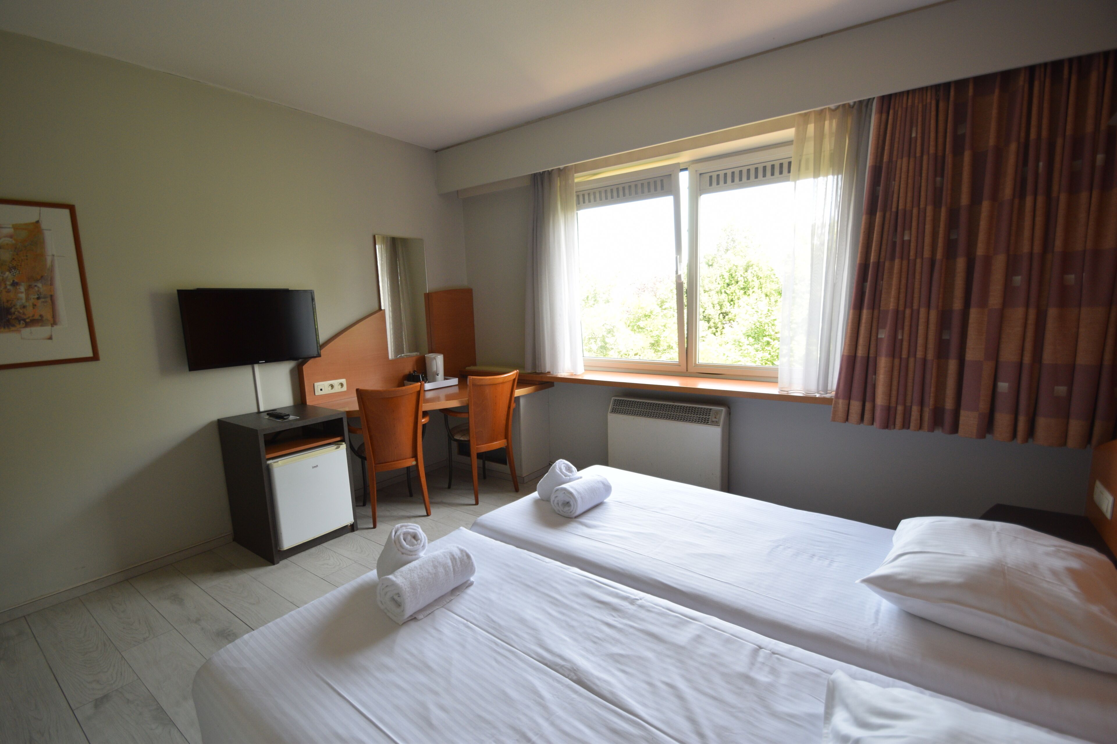 Une chambre d’hôtel avec deux lits, un bureau, une chaise, une télévision et une fenêtre avec des rideaux.