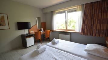 Une chambre d’hôtel avec deux lits, un bureau, une chaise, une télévision et une fenêtre avec des rideaux.