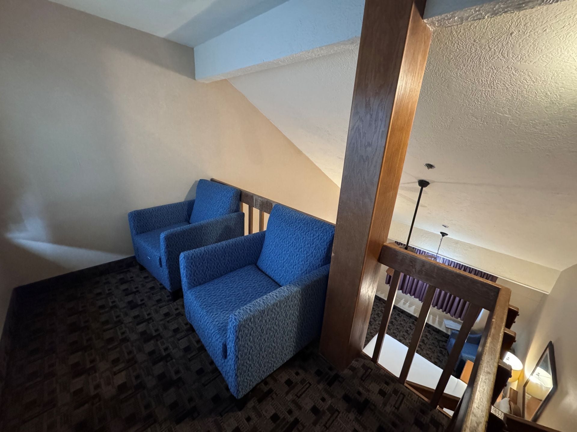 Una habitació amb un disseny de moqueta, un sofà tapissat de blau i una escala de fusta.