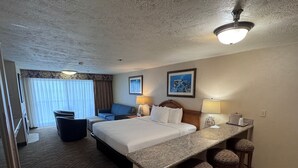 Habitación de hotel con cama, escritorio con taburetes, una silla, un sofá y vista al exterior.