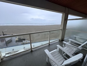 Un balcón con vista a la playa, sillas blancas y una barandilla.