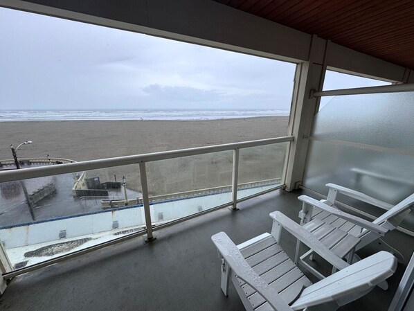 Un balcon donnant sur la plage, avec des chaises blanches et une balustrade.