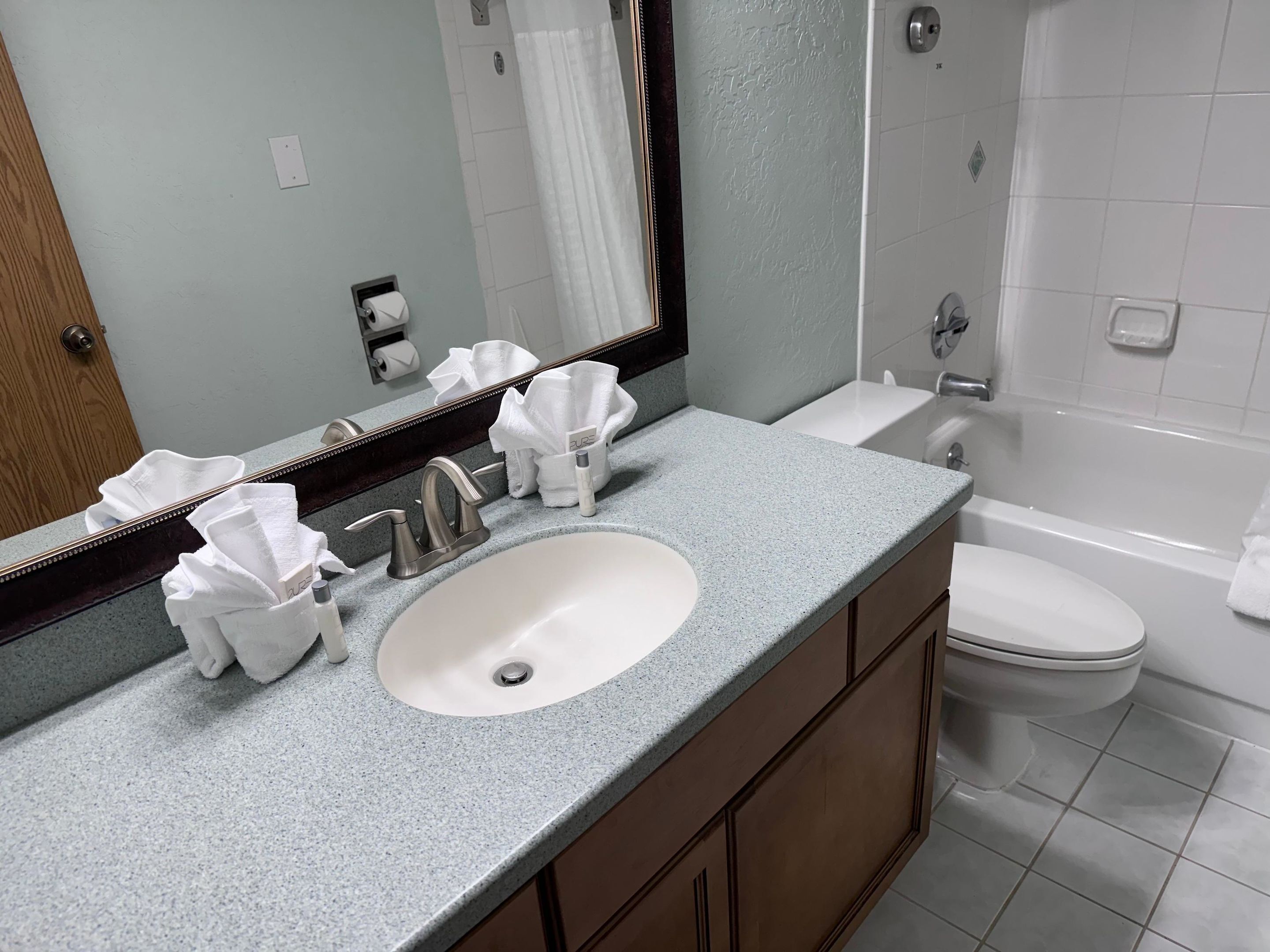 A bathroom with a sink, mirror, towel dispenser, and toilet.