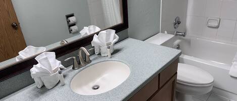A bathroom with a sink, mirror, towel dispenser, and toilet.