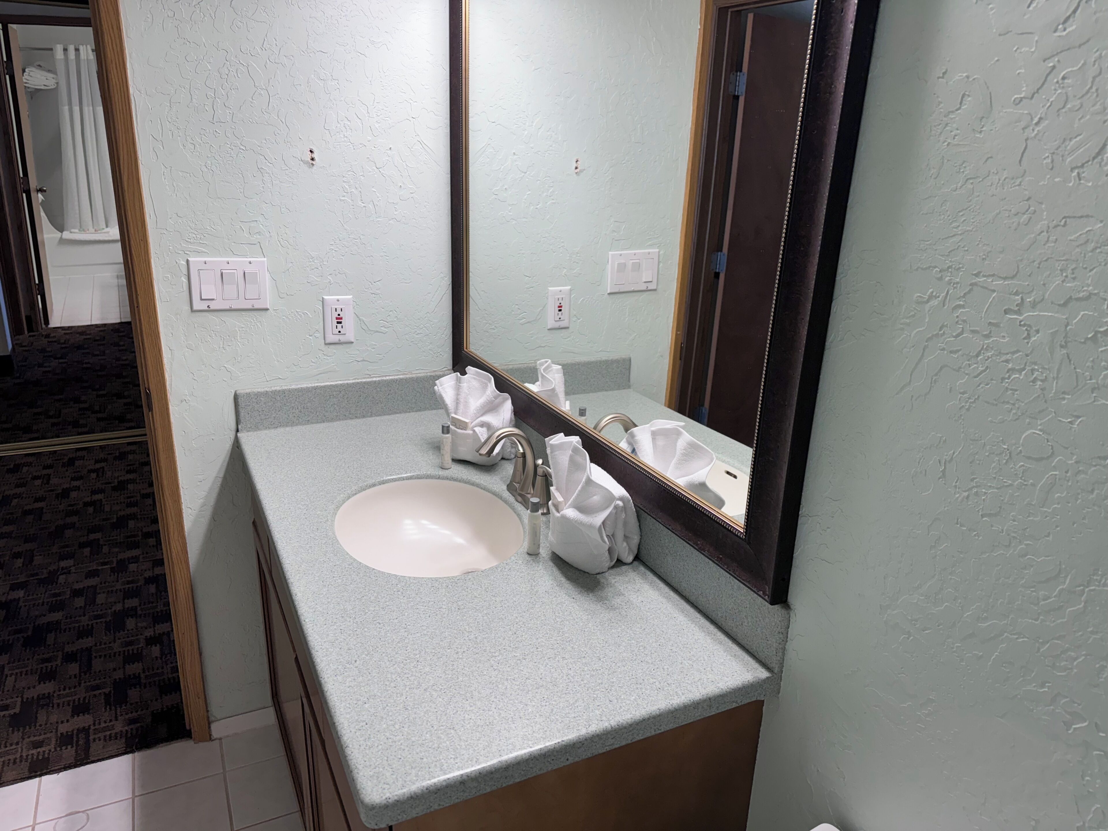 Un baño con un lavamanos blanco, un espejo y un perchero para toallas.