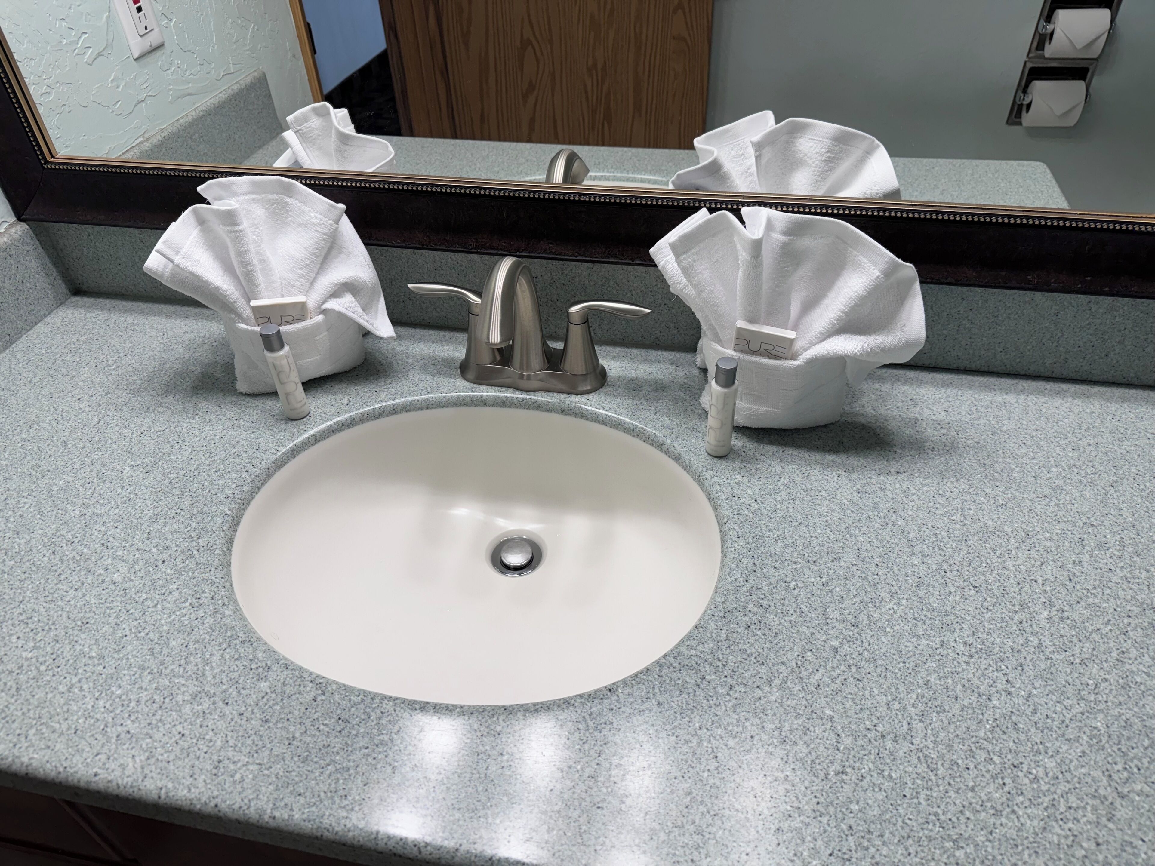 A bathroom sink with a mirror above it, a towel dispenser, and a soap dispenser.