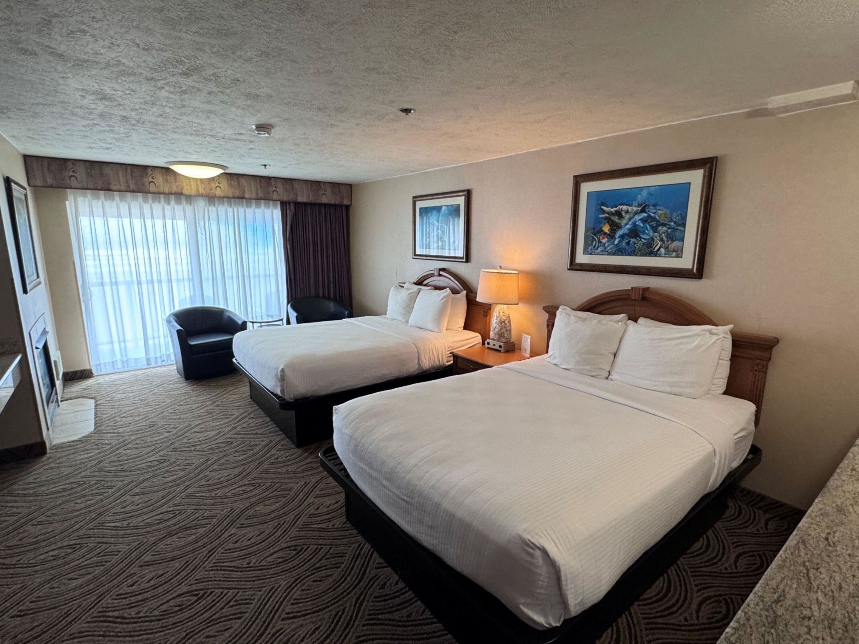 A hotel room with two beds, a desk, a chair, a lamp, and a painting on the wall.