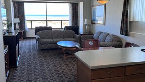 Habitación de hotel con sofá, mesa de comedor, kitchenette y ventana grande con vista a la playa.