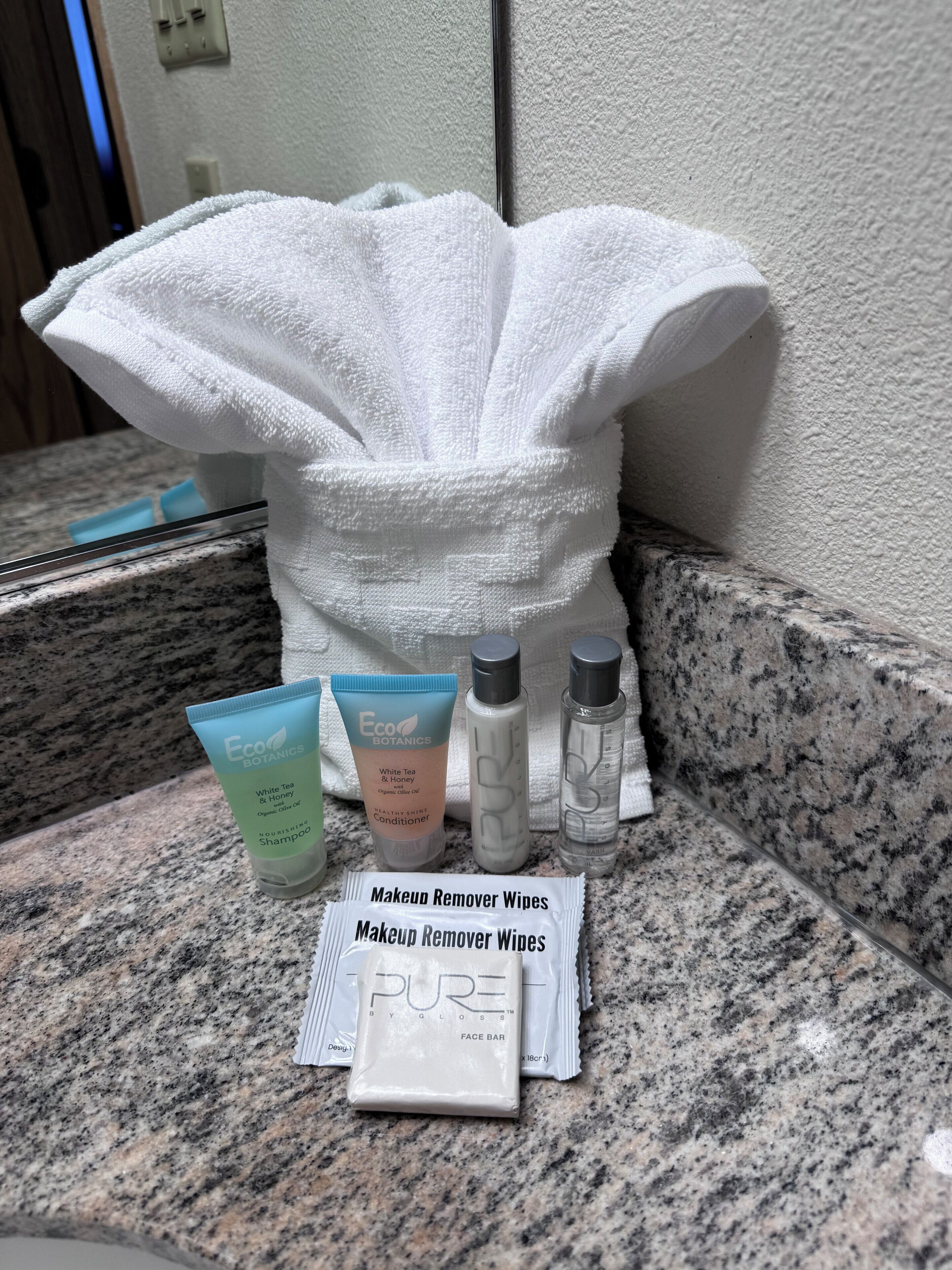 A bathroom counter with a white towel, a makeup remover wipes packet, and three bottles of skincare products.