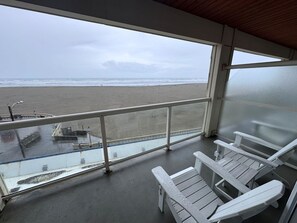 A balcony with a view of the beach, white chairs, and a railing.