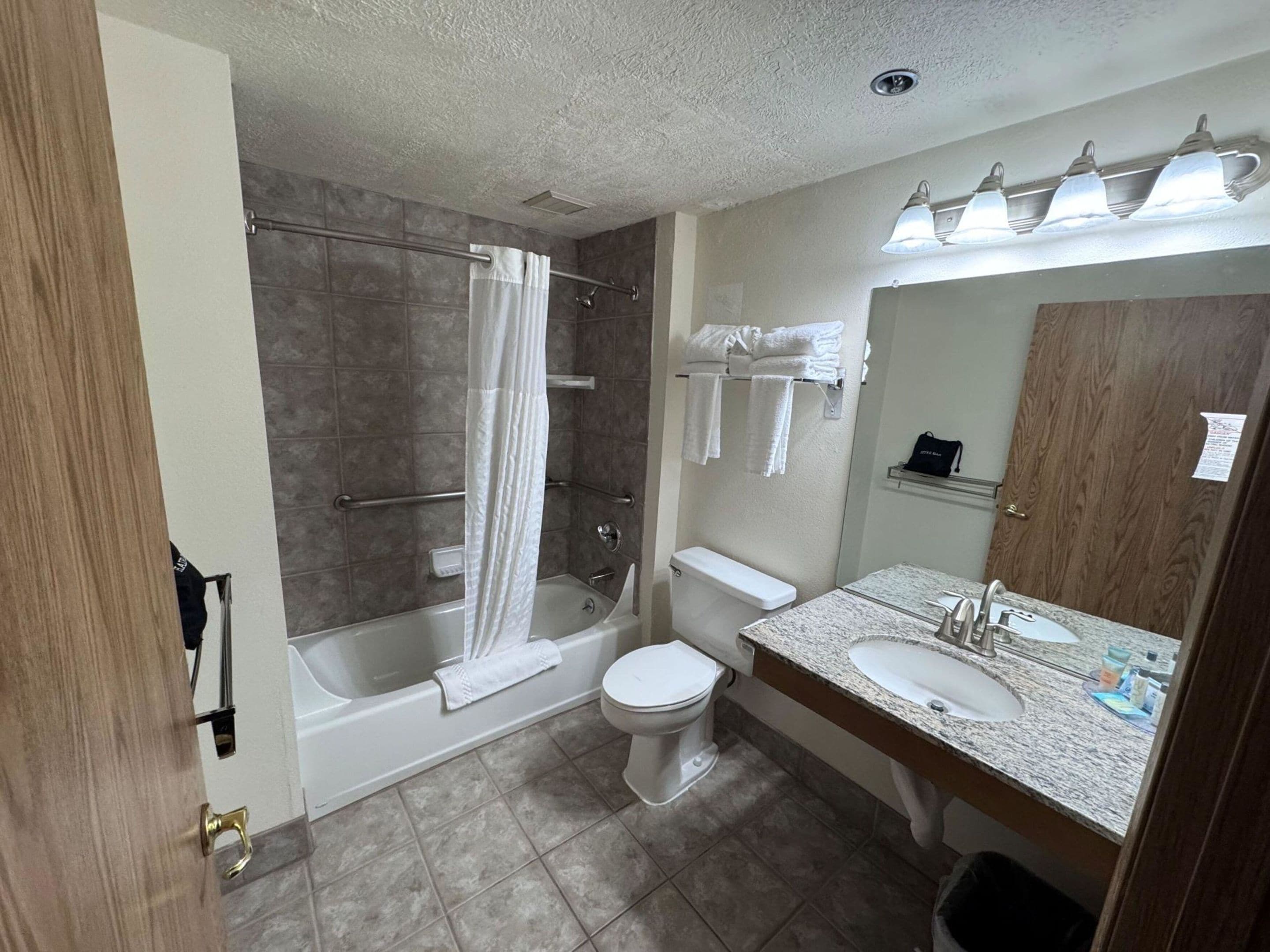 A bathroom with a bathtub, toilet, sink, and a mirror with lights.